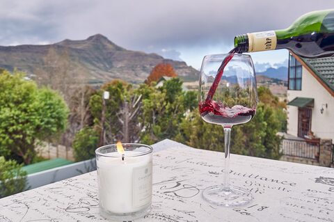 A glass of red wine poured beside a candle on the patio, with the Maluti Mountains behind